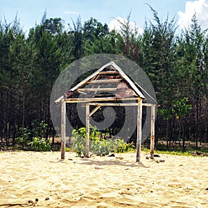 Old and rustic hut on the beach sand and trees behind