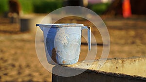Old rustic plastic watering mug holding on rough column. Blue empty mug closeup