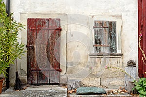 Old rustic vintage house front with massive wooden door and window shutters and flowers on the sides