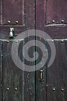 Old rustic wooden door with different layers of cracked paint  and hand knocker