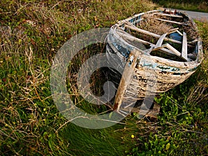 Old rustic wooden fishing boat ashore in the grass, damaged beyond repair