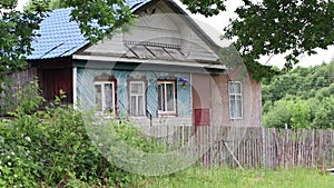 An old rustic wooden house stands behind a low fence.