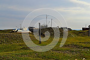 Old rusty abandoned boats, white ships lie on green grassy shore in the light of the sunset. Lake Baikal,