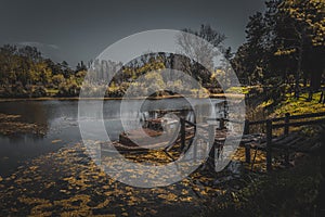 Old rusty abandoned wrecked ship tied up to a broken wooden dock in a small lake