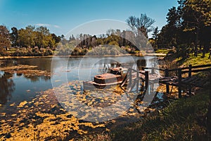 Old rusty abandoned wrecked ship tied up to a broken wooden dock in a small lake