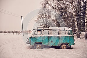 An old rusty ambulance van stands in a snow-covered clearing on a cloudy winter day