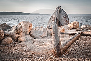 Old rusty anchor on the beach with stones