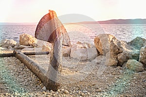 Old rusty anchor on the beach with stones
