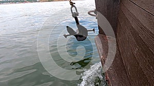 Old rusty anchor hanging rope, staggering near bow of stern floating wooden ship