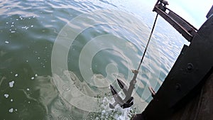 Old rusty anchor hanging rope, staggering near bow of stern floating wooden ship