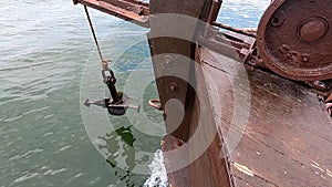 Old rusty anchor hanging rope, staggering near bow of stern floating wooden ship