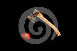 Old rusty axe hanging above red apple on a black background