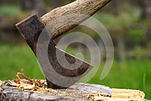 Old rusty axe with wooden handle stuck in the stump. blurred background with pile of wood logs, Large ax sticks out in