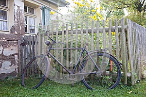 Old rusty bicycle leaning against wooden fence