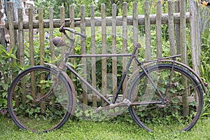 Old rusty bicycle leaning against a wooden fence