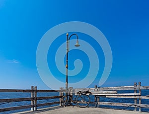 Old Rusty Bicycle Park Under The Damage Lamppost At The Wooden Pier of Marina Beside The Sea