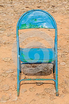 Old rusty blue chair leave alone in abandoned dried backyard.