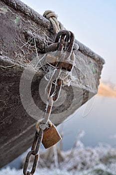 Old rusty boat covered with icing and webs,old rusty chain, lock and screw. Anchored rowboat in winter