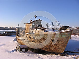 Old rusty boat moored to the shore in the winter froze on the river