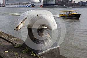 old rusty bollard in the port of Rotterdam with watertaxi in background