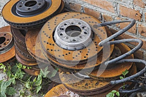 Old rusty brake discs lie in the grass near a brick wall