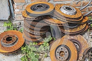 Old rusty brake discs spring and canister lie in the grass near a brick wall
