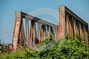Old rusty bridge over the river. Transportation. Old metal railway bridge. Steel bridge across the river against blue sky