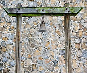 Old Rusty Bronze Metal Bell Hanged on A Green Mossy Wood  Pillar In A Stone Pattern Wall