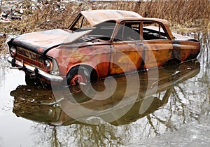 An old rusty car in a puddle arrived