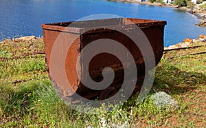 Old rusty coal tub on tracks, on the sea cliff in Megalo Livadi village, Serifos island, Greece