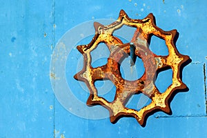 Old rusty cogwheel hanging on blue metal wall background