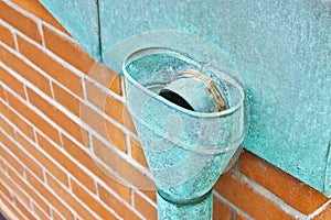 Old rusty copper downpipe against a brick wall