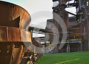 Old rusty cup for casting steel on a green field in an abandoned steelworks factory