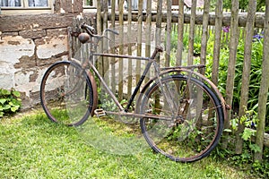 Old rusty damaged bicycle leaning at a wooden fence in a rural area
