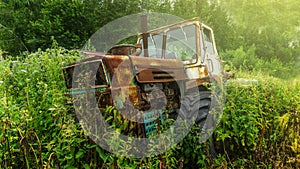 An old rusty derelict tractor parked in a farm yard in amongst overgrown grass and weeds