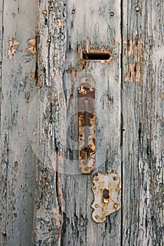 Old and rusty door knob with keyhole on pale and vintage blue wooden doors.