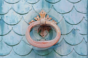 Old rusty door knocker on a teal painted door with a fish scales pattern