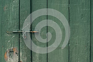 The old and rusty door latch and lock on green wooden door. Dark tone