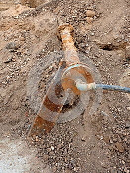 Old rusty drink waser pipe with flex member and plastic tube. Open excavation pit.