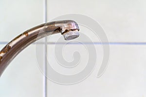 Old rusty drinking tap with a drop of water on a light background close-up.