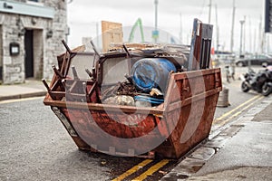 Old rusty dumpster skip in a street fool of rubbish and old furniture, Selective color. Nobody. Concept getting rid of old junk