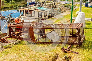 Old and rusty empty fishing trap, for lobsters or crabs next to a fishing boat on the pier of the port of Clifden