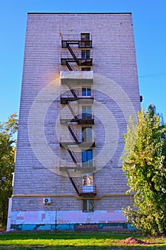 The old rusty fire escape to the floors is located near the wall of the building. House with metal staircase outside