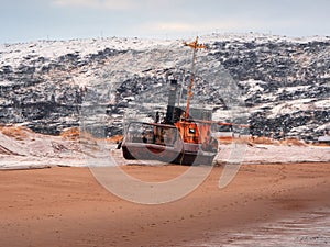 An old rusty fishing boat abandoned by a storm on the shore. Graveyard of ships, old fishing village on the shore of the Barents