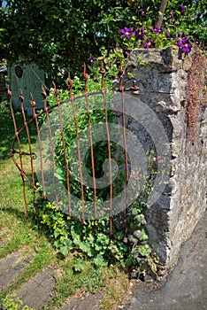 Old rusty garden gate and stone wall. West Tanfield, North Yorkshire.