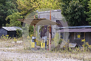 Old rusty gas station and dispensers abandoned and overgrown with vegetation on a sunny day. Summer