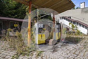 Old rusty gas station and dispensers abandoned and overgrown with vegetation on a sunny day. Summer