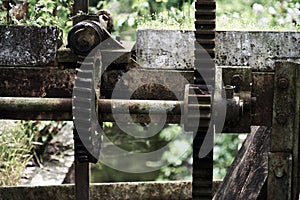 Old rusty, gears and racks on the gearbox of a historic weir at the outlet of a stream next to a watermill, dark, desaturated