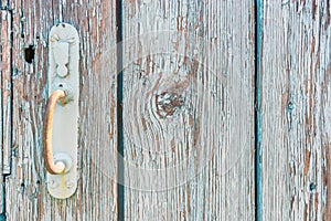 Old rusty handle on wooden door with cracked peeling blue paint close up. Texture of weathered painted wood with copy space for