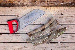 Old rusty handsaw over a wooden boards background with logs of cut firewood